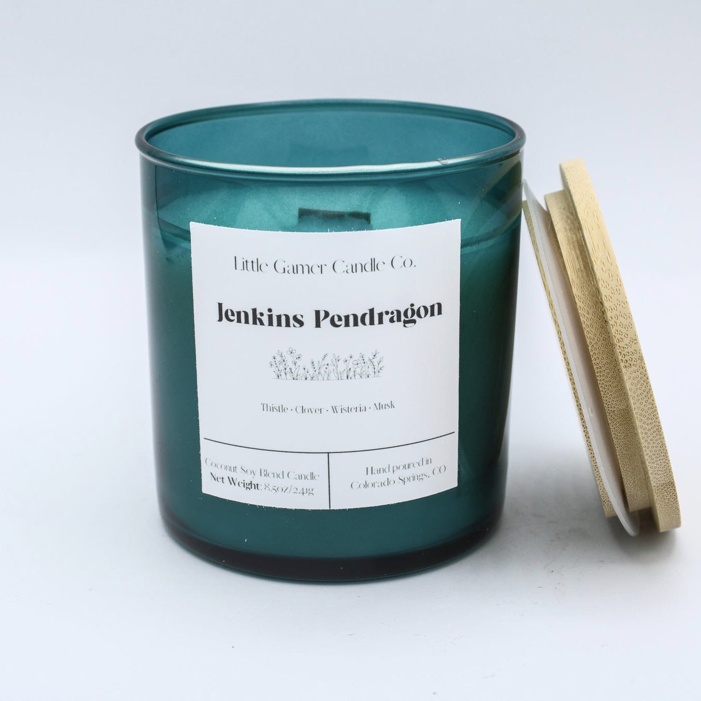 A teal glass jar candle with a white paper label reading 'Little Century Candle Co. Jenkins Pendragon' and a light wood lid leaning against the right side, photographed on a clean white background.