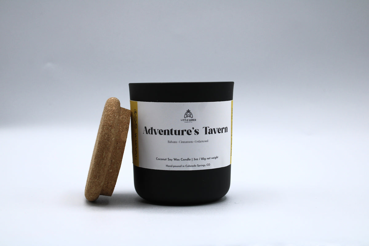 Candle with a cork lid labeled 'Adventure's Tavern' on a light gray background