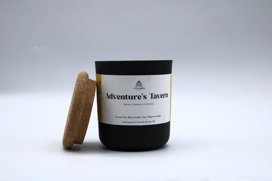 Candle with a cork lid labeled 'Adventure's Tavern' on a light gray background