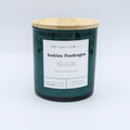 A dark green glass jar candle with a light bamboo wood lid and a white paper label reading 'Little Gassy Candle Co. jenkins Pendragon'.