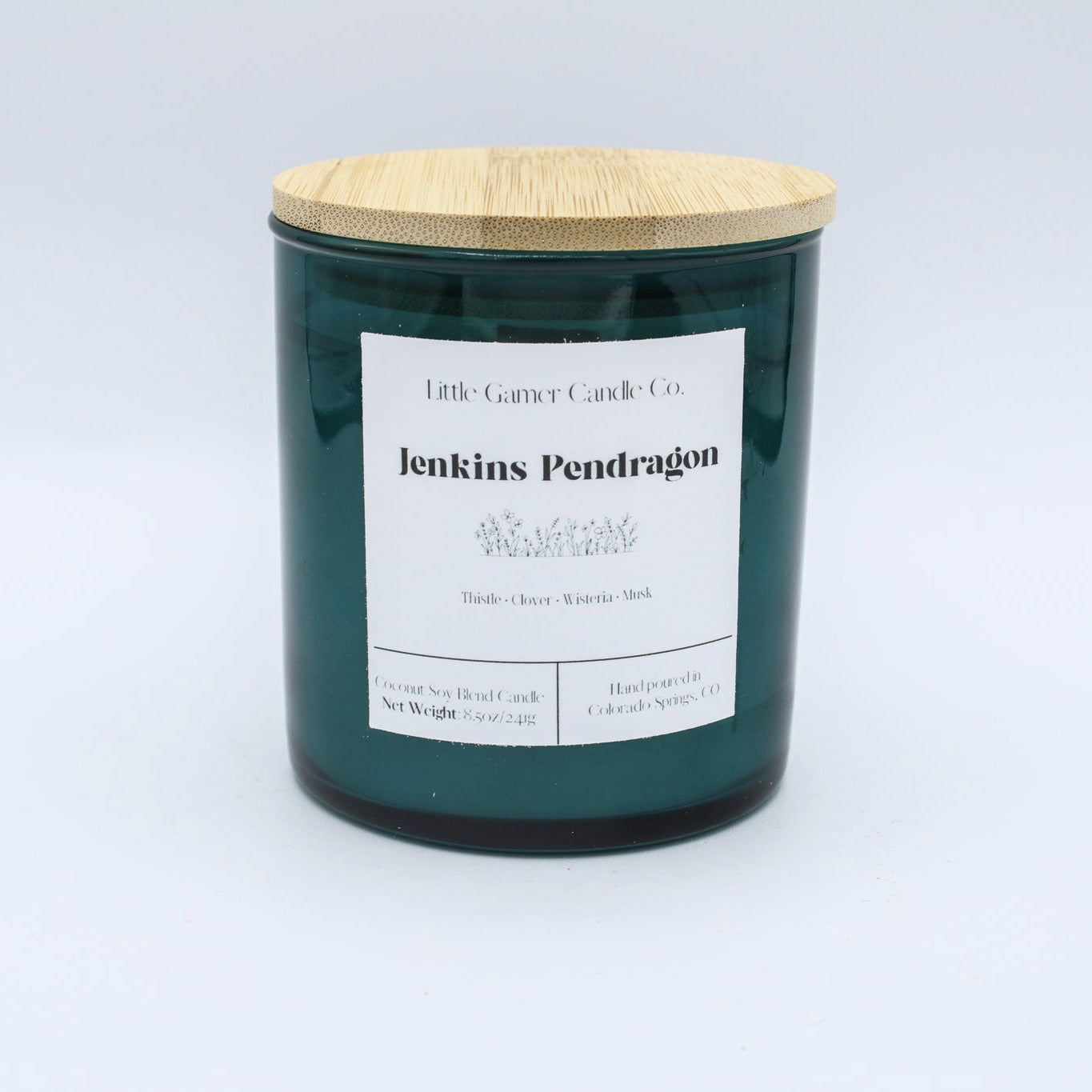 A dark green glass jar candle with a light bamboo wood lid and a white paper label reading 'Little Gassy Candle Co. jenkins Pendragon'.