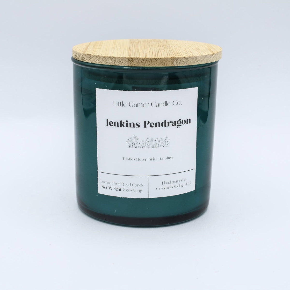 A dark green glass jar candle with a light bamboo wood lid and a white paper label reading 'Little Gassy Candle Co. jenkins Pendragon'.
