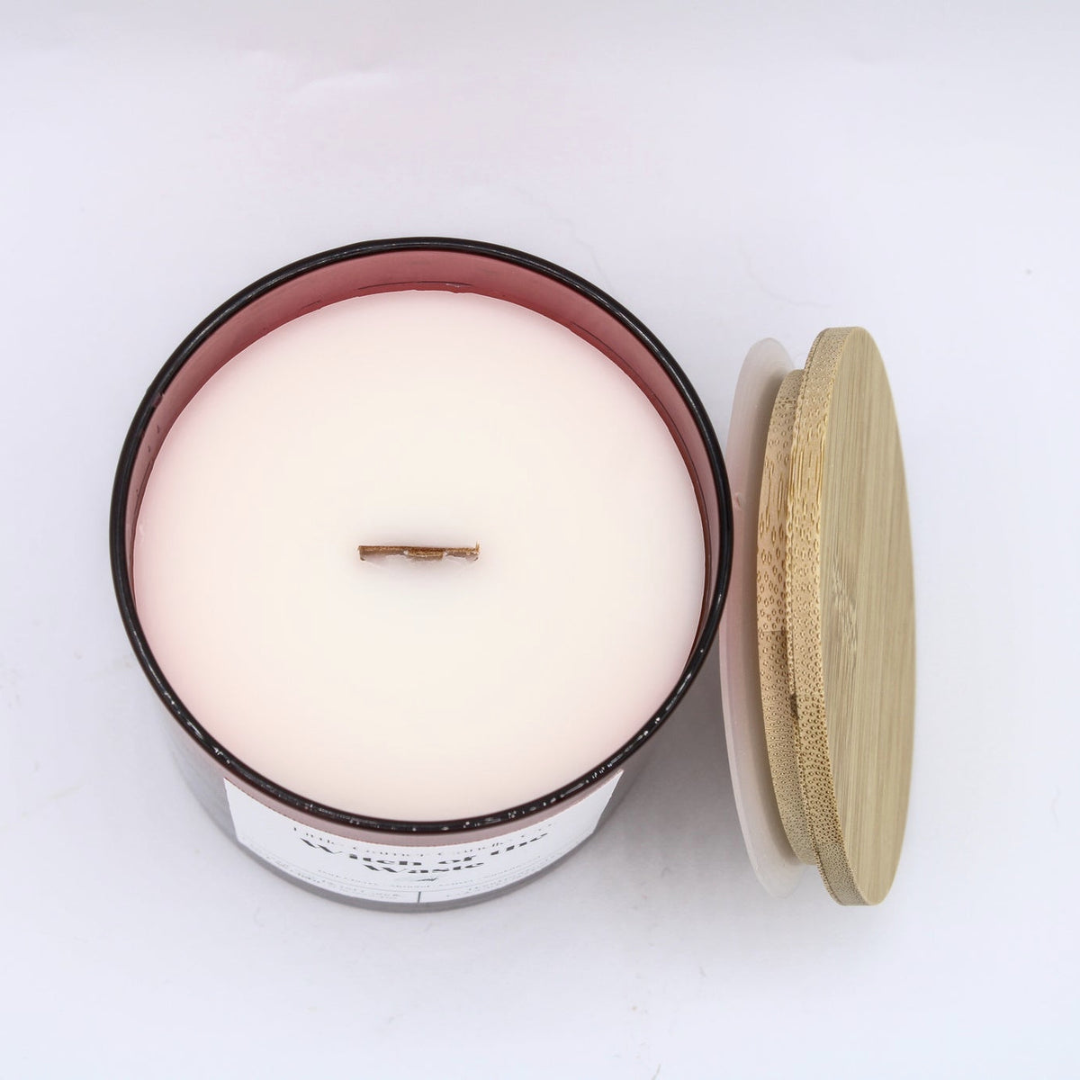 An open jar candle with pale cream wax and a single wick, shown next to its light wood lid on a plain white background.