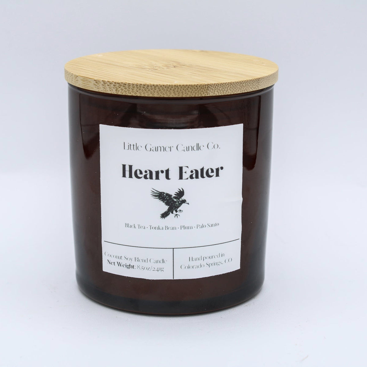A dark amber glass jar candle with a light bamboo lid and a white label reading 'Little Goat Candle Co. Heart Eater' on a white background.