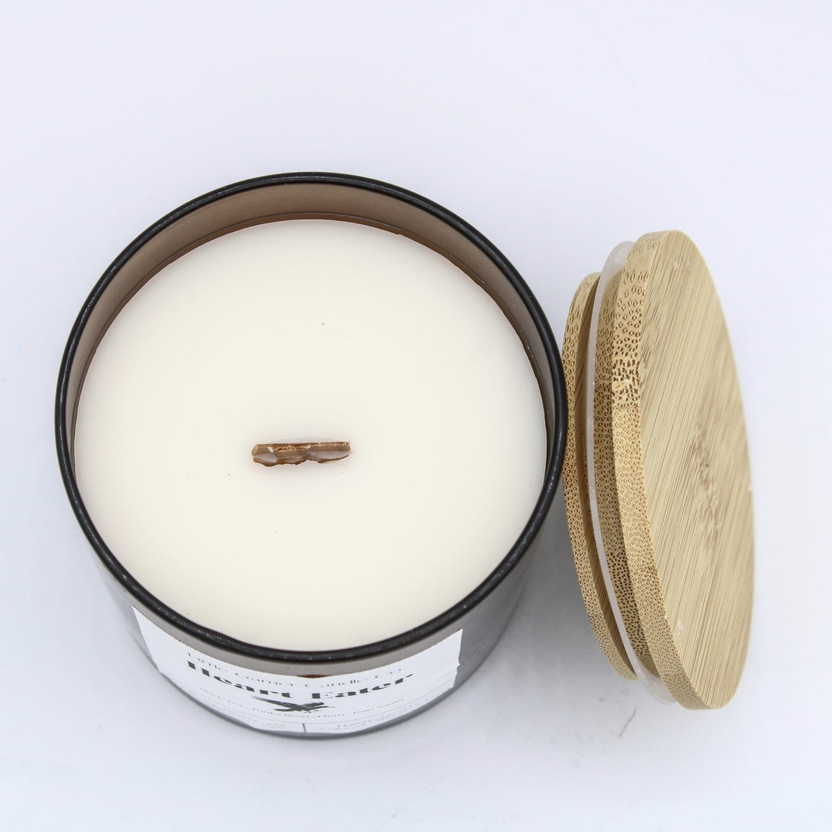 An open jar candle with creamy off-white wax and a single wick, shown next to a light natural bamboo lid on a plain white background.