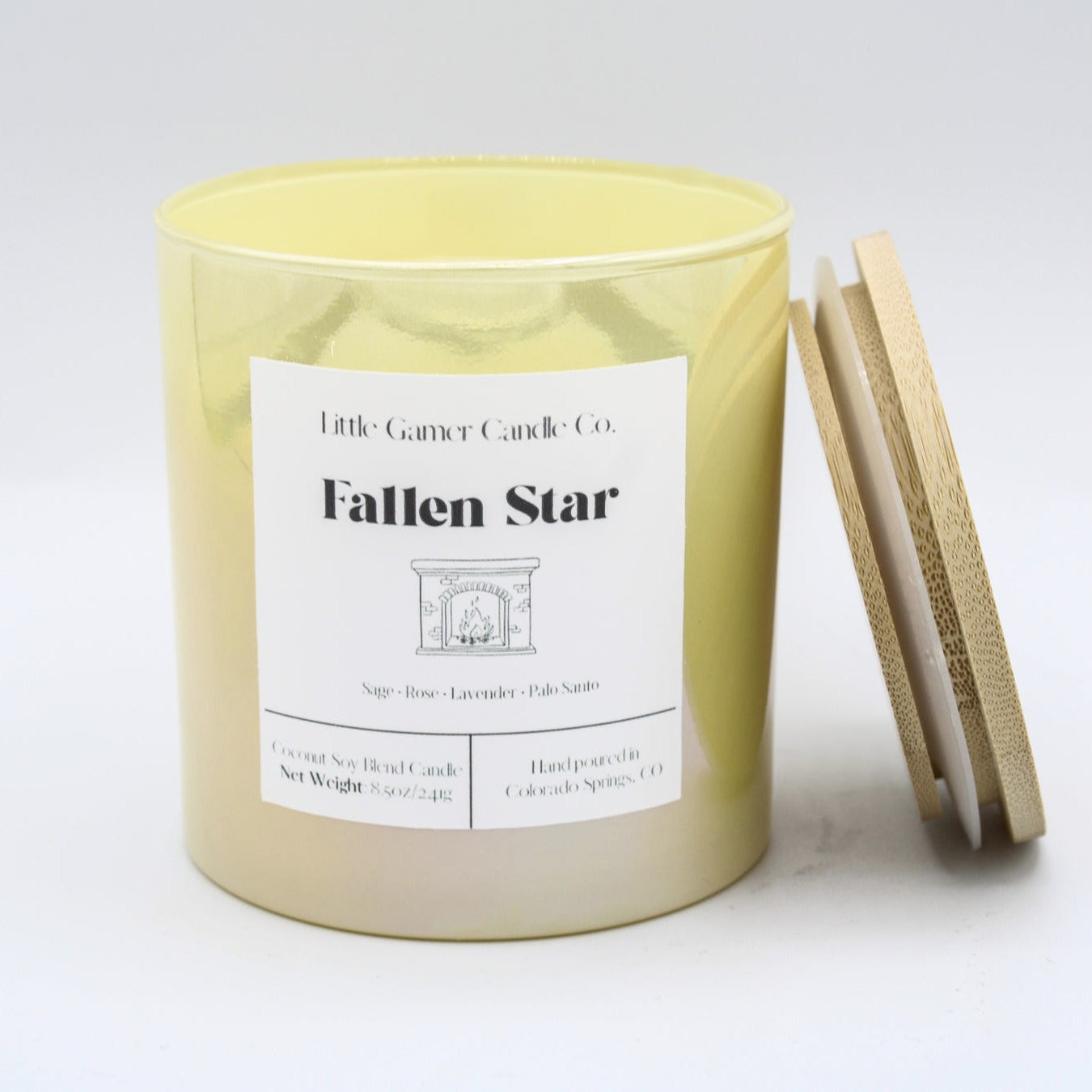 A yellow soy wax candle in a cylindrical glass jar with a white label reading 'Little Candles Candle Co. Fallen Star,' shown with a wooden lid leaning against the jar on a white background.